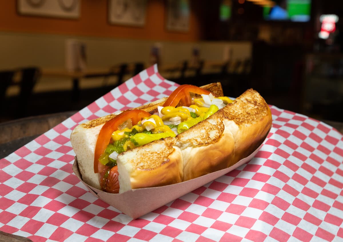 Al Capone - All-beef hot dog with yellow mustard, neon relish, chopped onions, tomato, pickle, sport peppers, and celery salt on a Hawaiian roll.