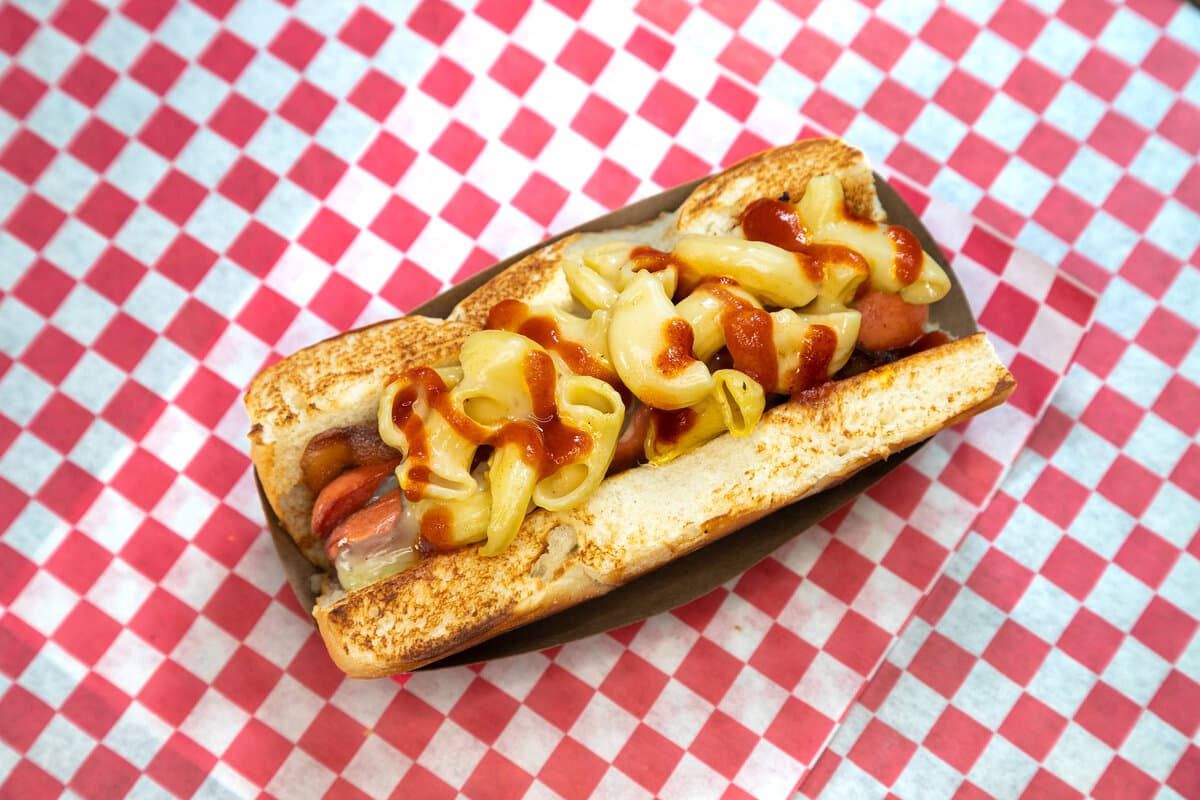 Say Cheese - All beef frank wrapped in bacon and covered with house made mac n' cheese and Sriracha sauce served on A Hawaiian roll